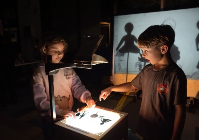 Two children creating a shadow puppet show using an overhead projector.