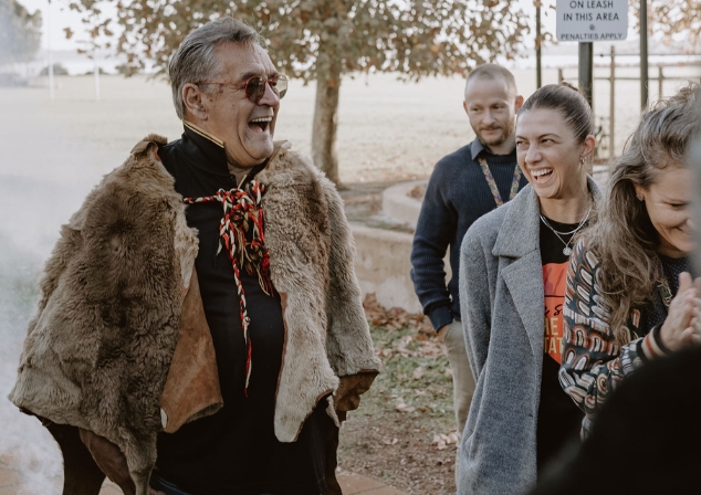 Aboriginal Elder, Uncle Neville Collard, standing next to three people laughing, with smoke from smoking ceremony in the background.