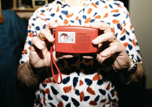Two hands holding a small red radio from the Museums Collection