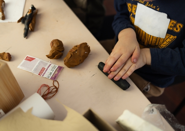 A picture of a child's hands working a piece of moulding clay on a table amongst other craft materials.