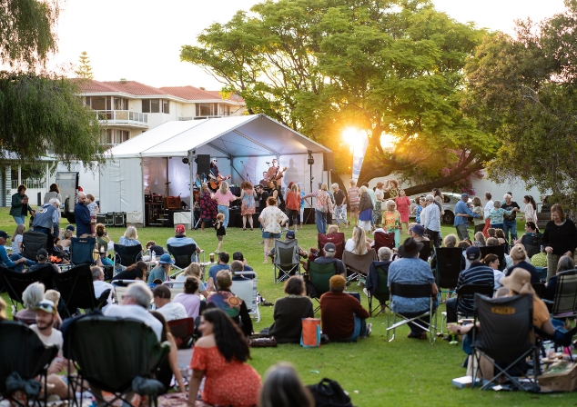 Crowd of people at sunset watching and dancing to a band in a marquee on a grassed lawn.
