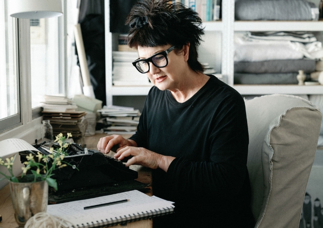 Woman dressed in black sits in an office, typing on an old black typewriter.