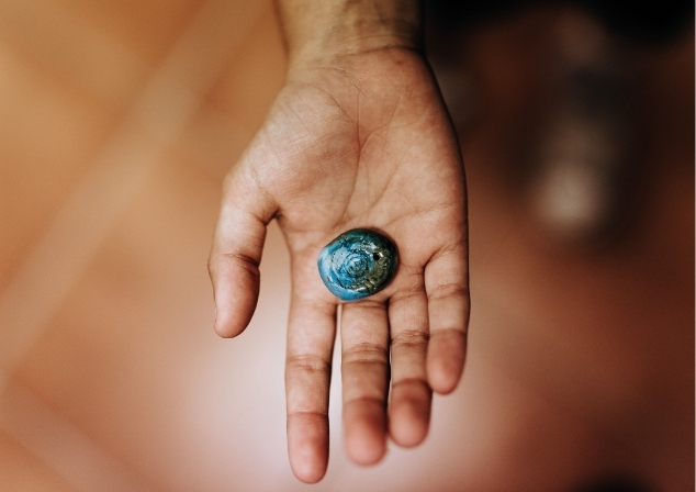 An open hand outstretched with the palm holding a small blue shell.