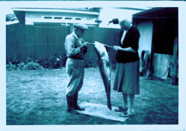 An historic photograph of an older couple in a backyard holding a very large fish on a wooden rod.