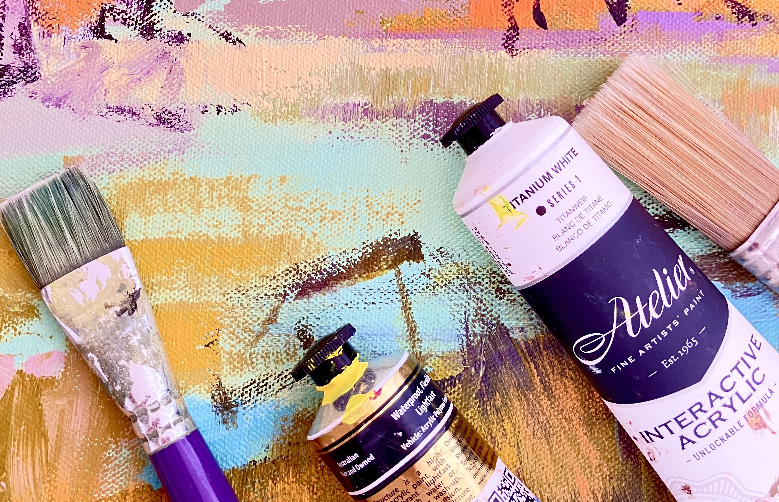 Paintbrushes and paint tubes over a canvas of acrylic.