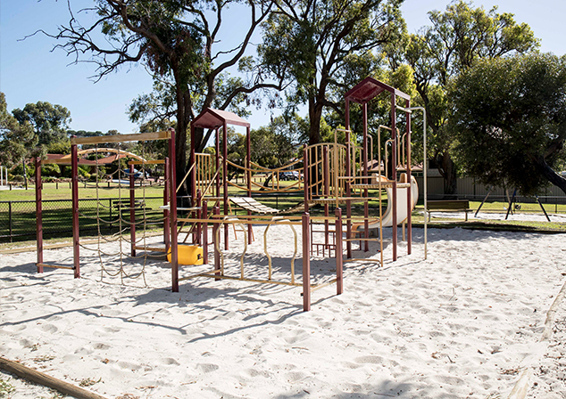 Children's playground in sand pit with tall trees surrounding