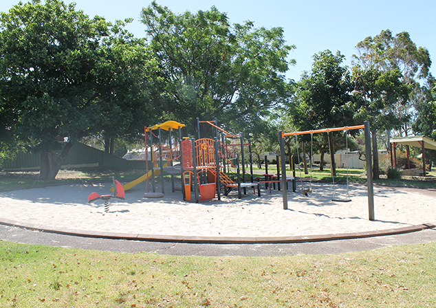 Children's playground in sand pit with tall trees surrounding