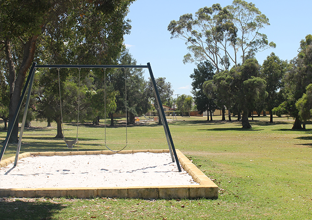 Grassed area with tall tress and children's playground