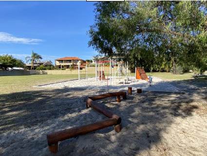 Children's playground in sandpit with grassed area and tall trees