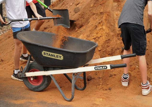 Group of three people shovelling a pile of dirt into a wheelbarrow.