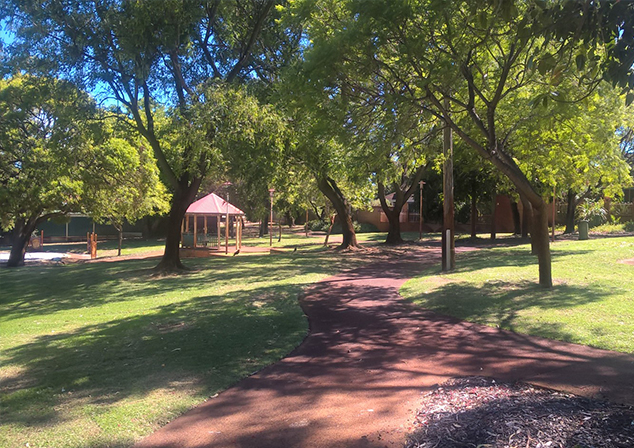 Footpath through tall tress and grass with a gazebo .