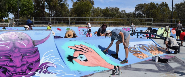 A skate park being painted with street art by a group of people.