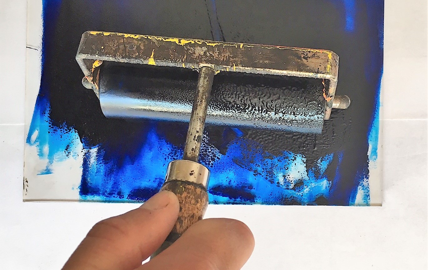 A hand with a printmaking press pressing ink.