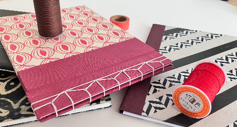 Three books with different patters stacked together with two spools of string.