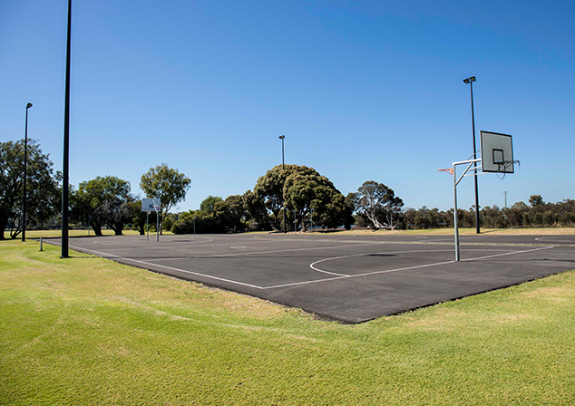 Photo of basketball/netball court, surrounded by grass field.