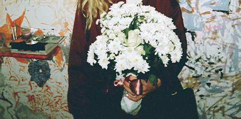 A photo of a person holding a bouquet of white flowers with abstract painting on the wall in the background.