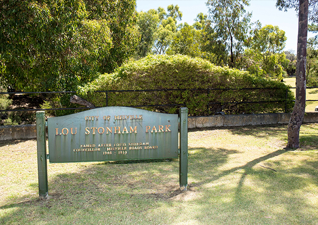 Park sign on grassed area with tress and fence behind