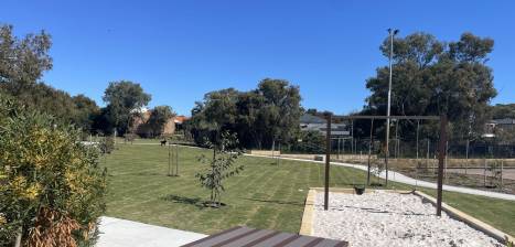 A park with a sandpit and swing on a sunny day 
