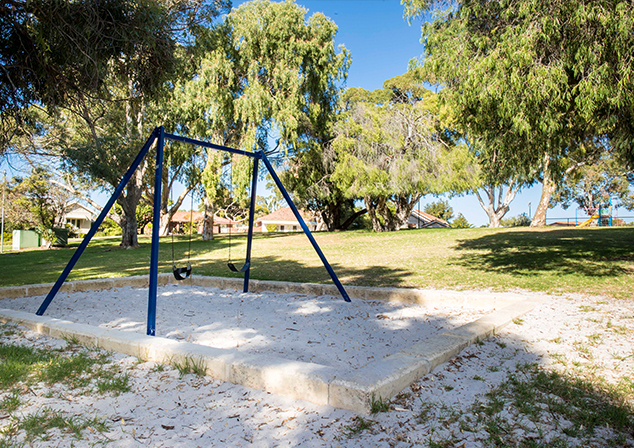 Children's playground in sand pit with tall trees surrounding
