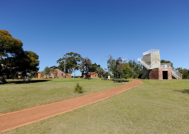 Wide photo of grassy area with a tower to the right and other buildings in distance to the left.