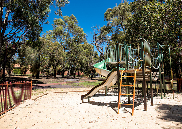 Children's playground in sand pit with tall trees surrounding 