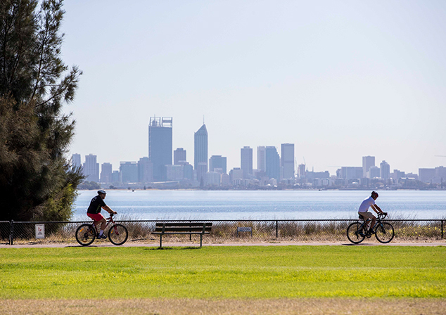 photo of people cycling along attadale foreshore with a view of perth city in the background
