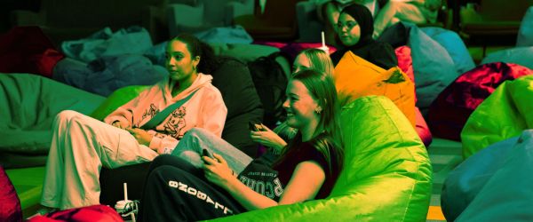 three young people sit on beanbags playing video games at the library.