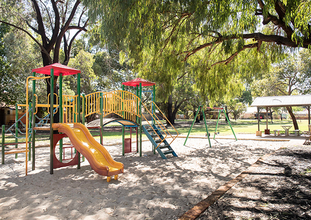 Children's playground in sand pit with tall trees surrounding