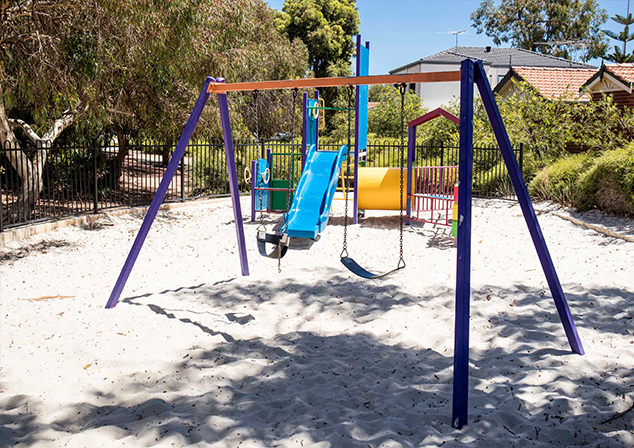 Children's playground in sand pit with tall trees surrounding
