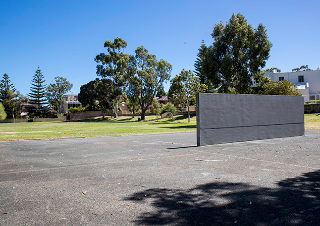 Paved area with grass and tall trees behind it